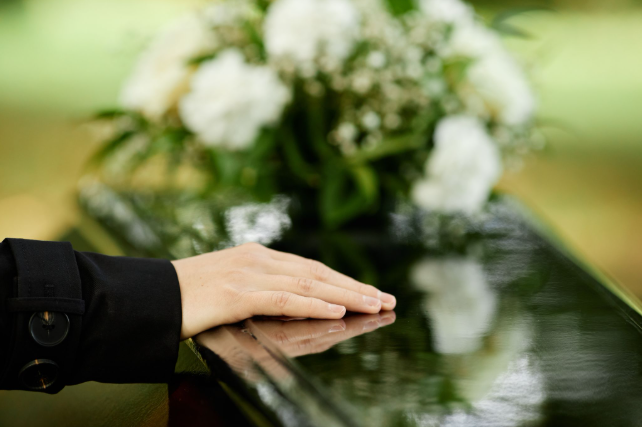 a person putting a hand on top of a coffin during a funeral