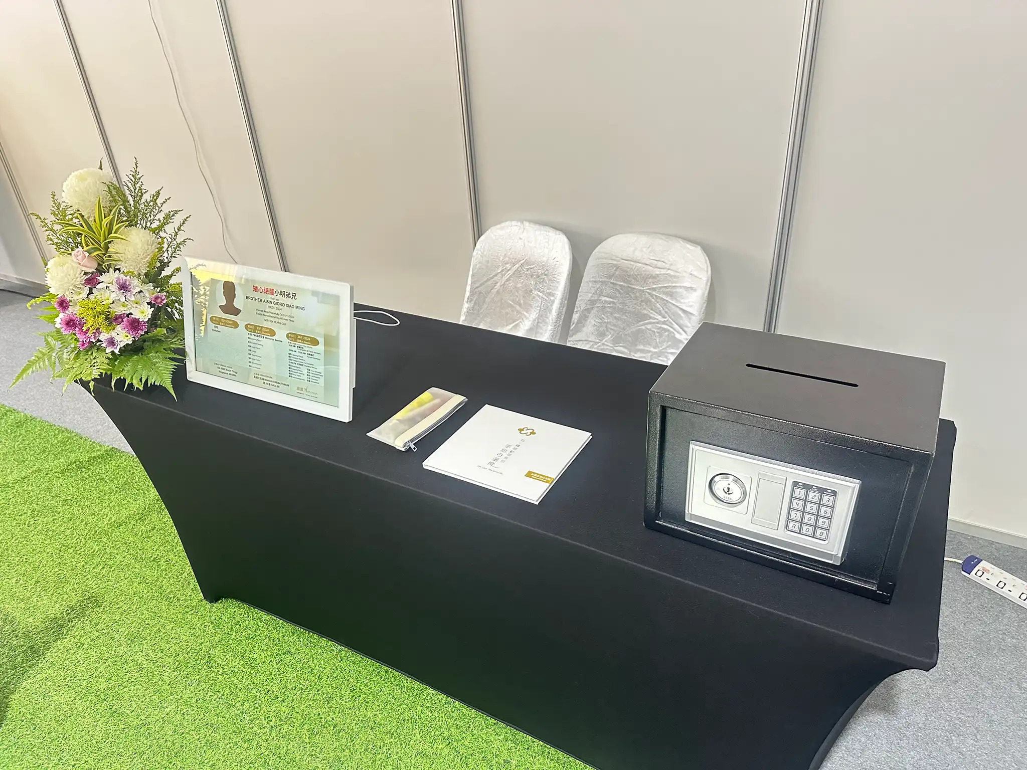 funeral reception counter with black tablecloth, safe box, framed photo display, and floral arrangement