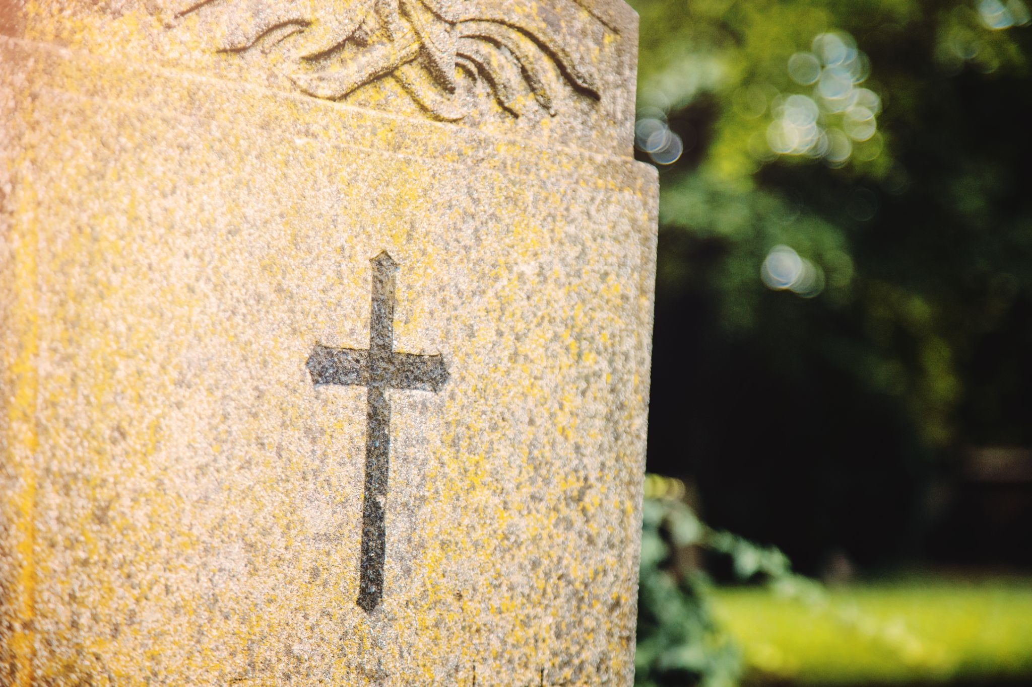 close-up of a stone gravestone featuring an engraved christian cross against a blurred cemetery background