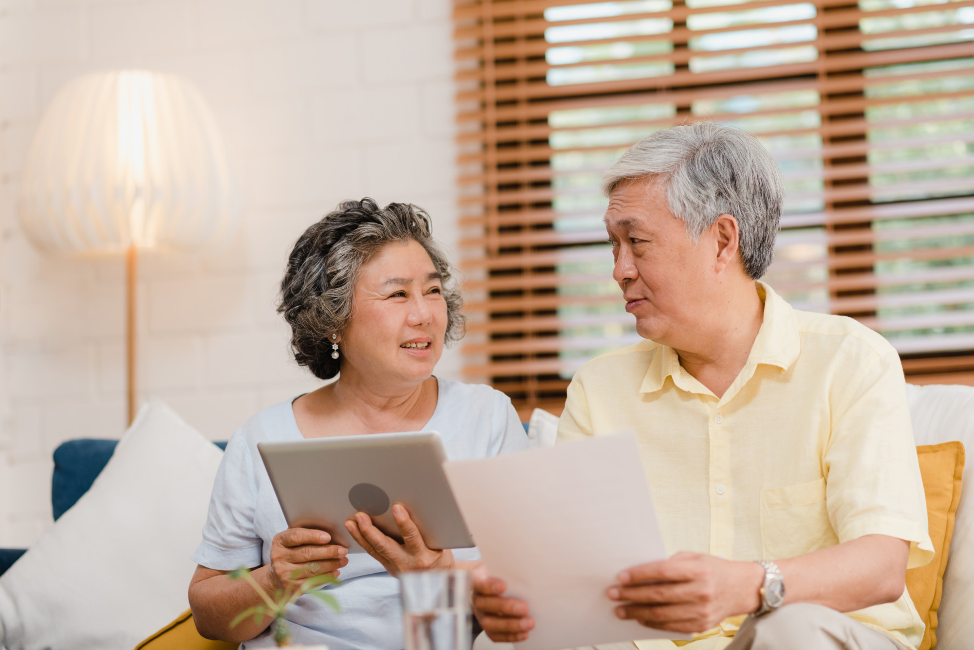 two senior citizens discussing over something while holding a tablet and a piece of paper